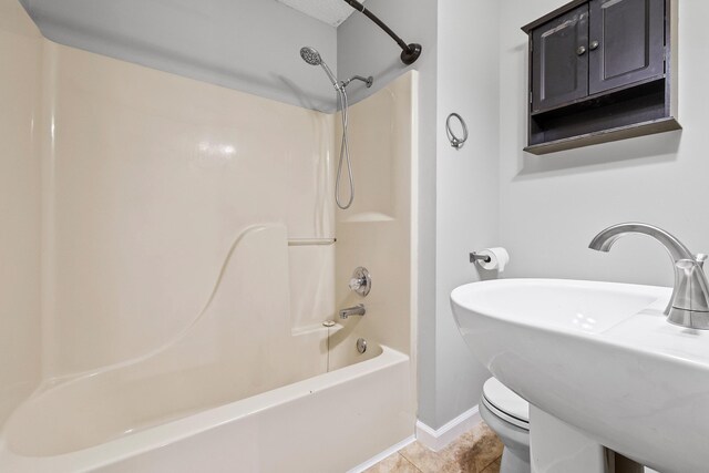 bathroom featuring shower / tub combination, toilet, a sink, baseboards, and tile patterned floors