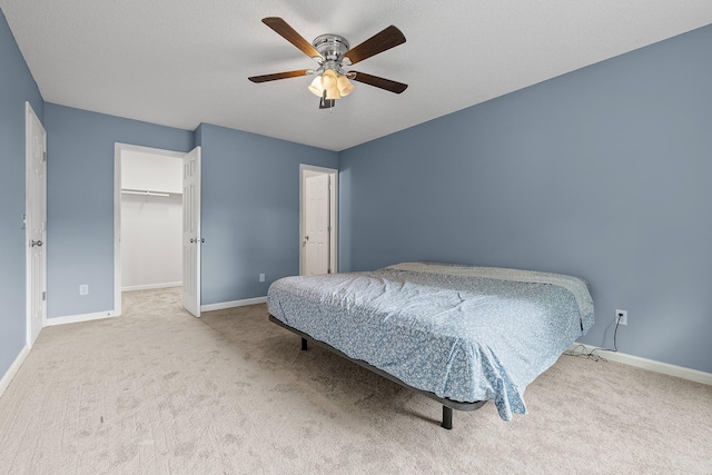 carpeted bedroom featuring ceiling fan, a spacious closet, baseboards, and a textured ceiling