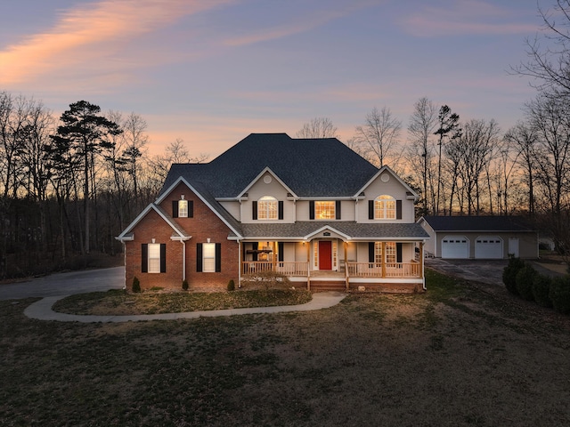 traditional home with a shingled roof, a porch, an outdoor structure, a front lawn, and brick siding