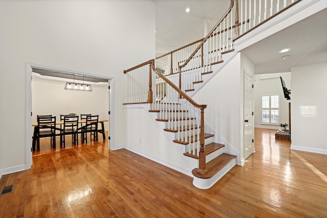 stairway with a towering ceiling, baseboards, wood finished floors, and recessed lighting