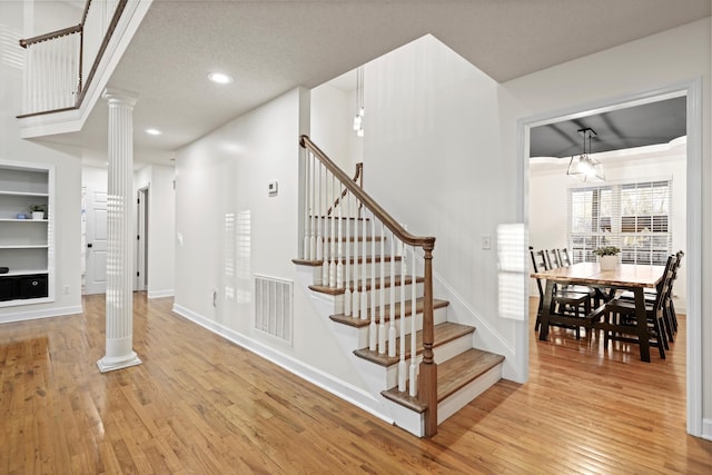 stairway featuring decorative columns, visible vents, wood-type flooring, and baseboards