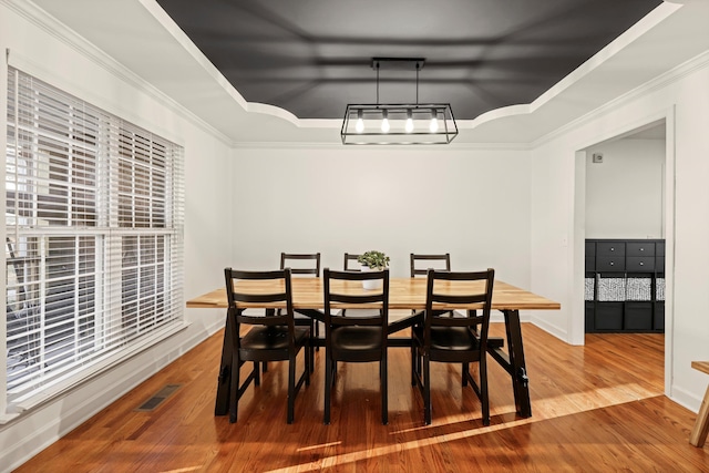 dining area with hardwood / wood-style floors, a tray ceiling, ornamental molding, and visible vents