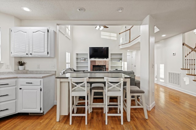 kitchen with a kitchen bar, visible vents, light wood finished floors, and white cabinetry