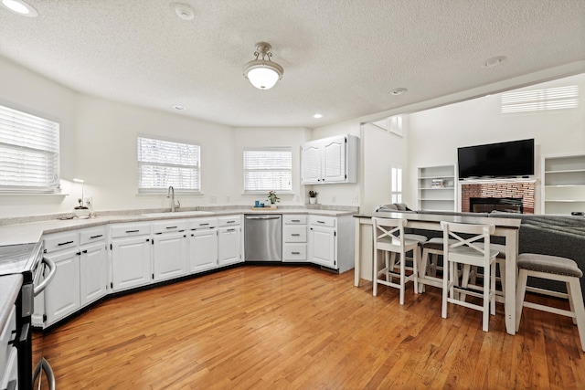 kitchen featuring stainless steel appliances, a sink, white cabinetry, a brick fireplace, and light wood finished floors