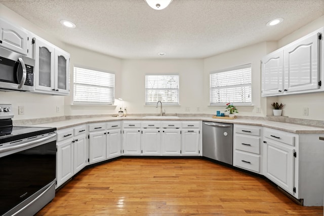 kitchen with stainless steel appliances, light wood finished floors, a sink, and white cabinets