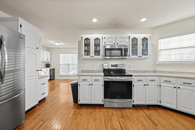 kitchen featuring light wood finished floors, white cabinets, glass insert cabinets, appliances with stainless steel finishes, and light countertops