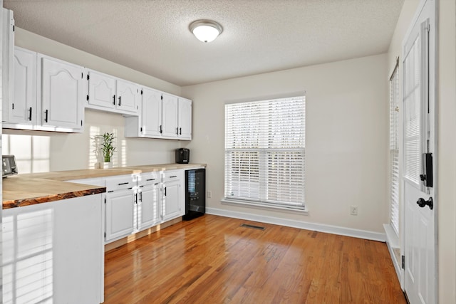 kitchen featuring wine cooler, wood counters, baseboards, white cabinets, and light wood-type flooring