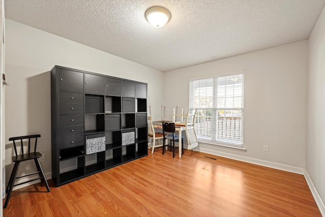 home office featuring baseboards, a textured ceiling, visible vents, and light wood-style floors