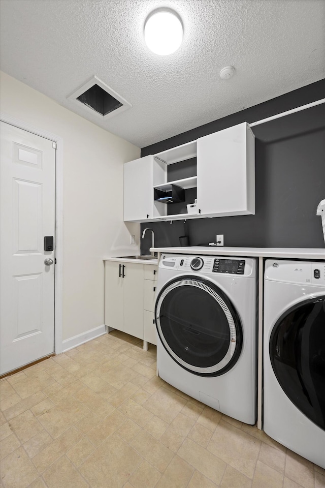 laundry room featuring washing machine and clothes dryer, cabinet space, a sink, a textured ceiling, and baseboards