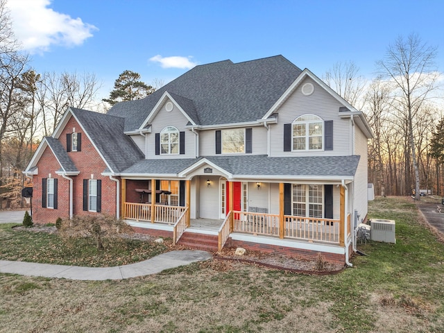 traditional-style home with covered porch, central AC, brick siding, roof with shingles, and a front lawn