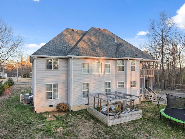 back of house featuring a shingled roof, a vegetable garden, crawl space, a trampoline, and a yard