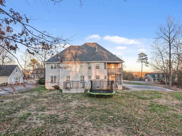 back of house featuring a balcony, a shingled roof, a trampoline, and a yard