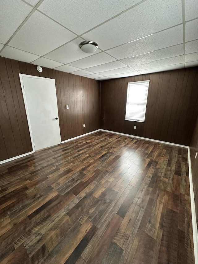 spare room featuring dark wood-style floors, a drop ceiling, wooden walls, and baseboards