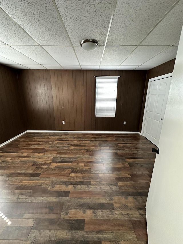 empty room with wood walls, wood finished floors, a paneled ceiling, and baseboards