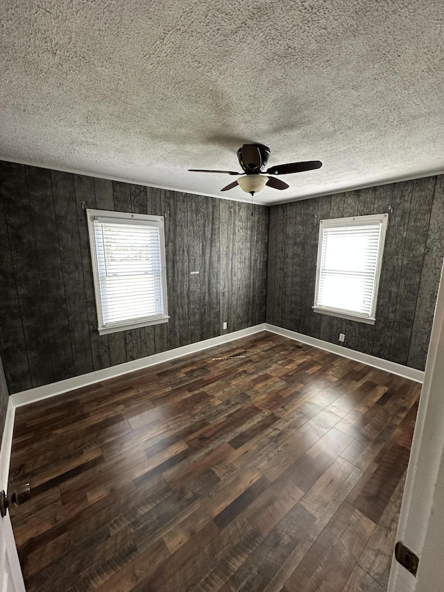 empty room with a wealth of natural light, a textured ceiling, baseboards, and dark wood-style flooring