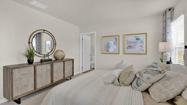 bedroom with ensuite bath, visible vents, baseboards, and light colored carpet