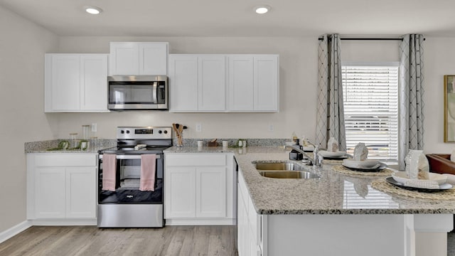 kitchen with appliances with stainless steel finishes, a sink, white cabinetry, and light stone countertops