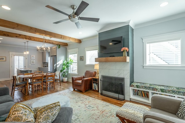 living room featuring baseboards, a tiled fireplace, beamed ceiling, wood finished floors, and crown molding