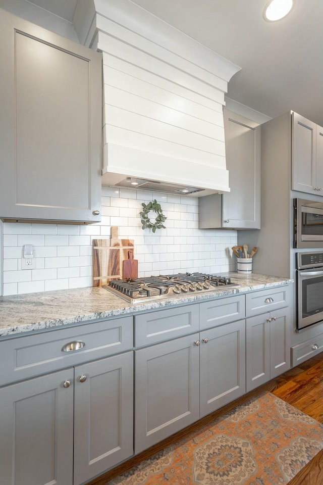 kitchen with stainless steel appliances, premium range hood, backsplash, and gray cabinetry