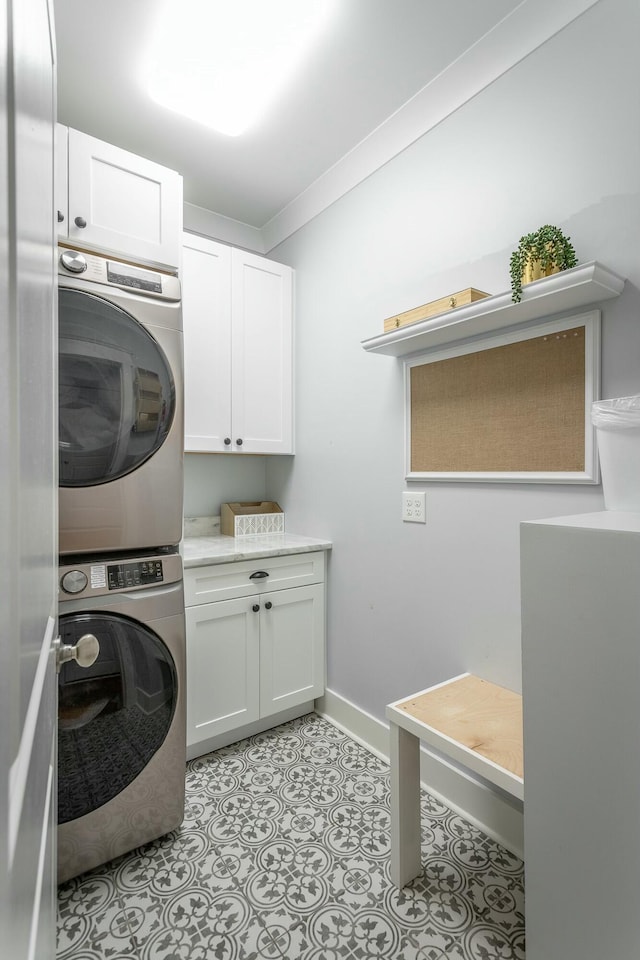 laundry room featuring cabinet space, baseboards, stacked washer / dryer, crown molding, and light tile patterned flooring