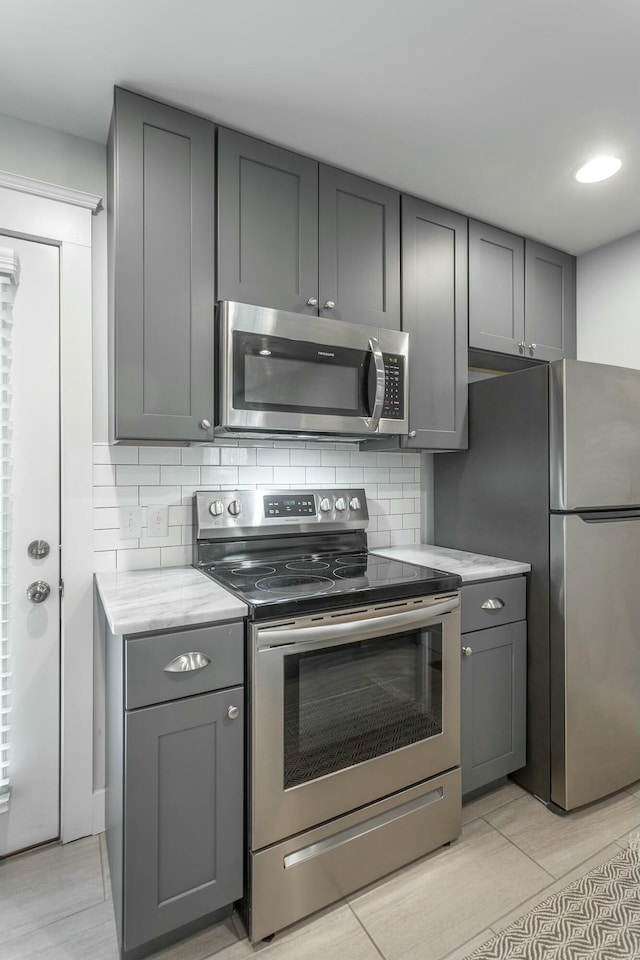 kitchen with stainless steel appliances, decorative backsplash, light stone countertops, and gray cabinetry