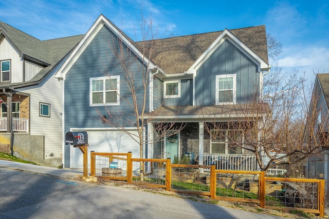 view of front of property featuring a porch, a fenced front yard, a garage, a shingled roof, and board and batten siding