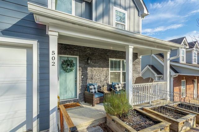 property entrance featuring stone siding, a porch, board and batten siding, and an attached garage