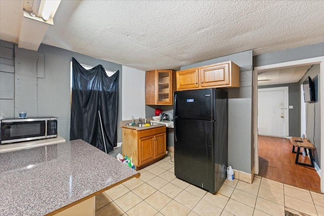 kitchen with stainless steel microwave, glass insert cabinets, light tile patterned floors, freestanding refrigerator, and a sink