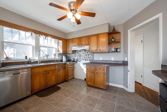 kitchen with brown cabinetry, dishwasher, under cabinet range hood, and a sink