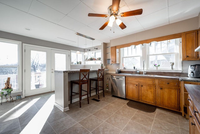 kitchen featuring a peninsula, stainless steel dishwasher, a sink, and brown cabinets