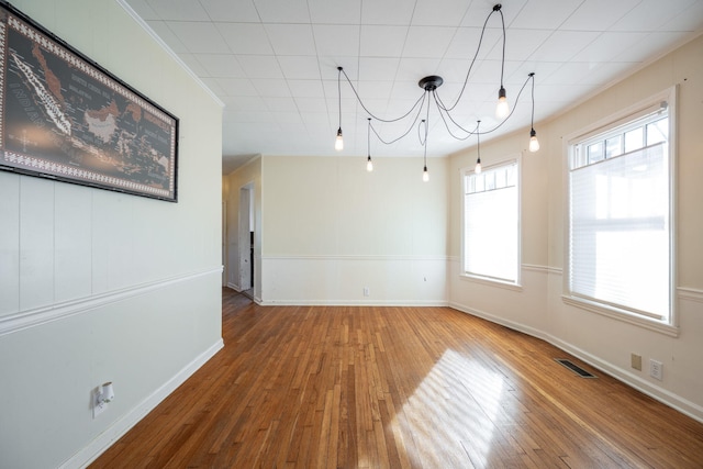 empty room with visible vents, crown molding, baseboards, and hardwood / wood-style flooring