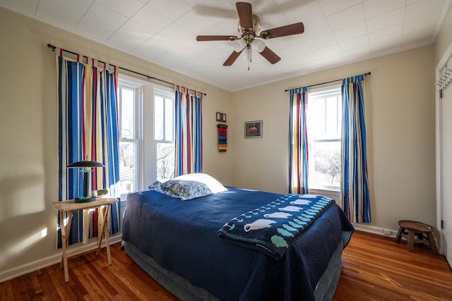 bedroom featuring a ceiling fan, crown molding, baseboards, and wood finished floors