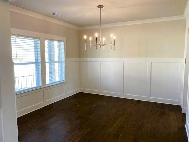 unfurnished dining area featuring dark wood-style floors, visible vents, a decorative wall, an inviting chandelier, and ornamental molding