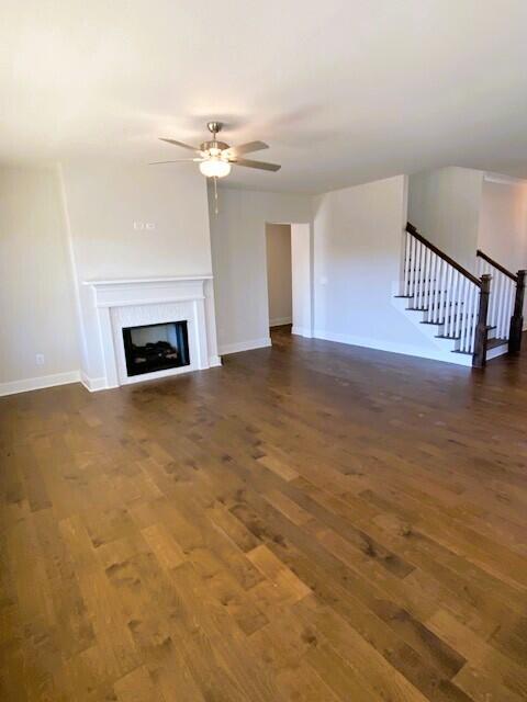 unfurnished living room featuring baseboards, a ceiling fan, stairway, wood finished floors, and a fireplace