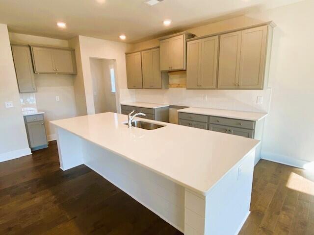 kitchen with gray cabinets, dark wood-style flooring, a sink, and a center island with sink