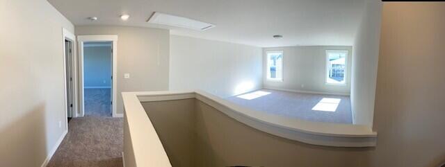 hallway featuring attic access, carpet, baseboards, and an upstairs landing