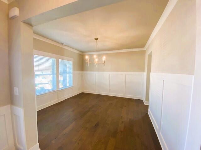 unfurnished dining area featuring a decorative wall, dark wood-style flooring, wainscoting, an inviting chandelier, and crown molding