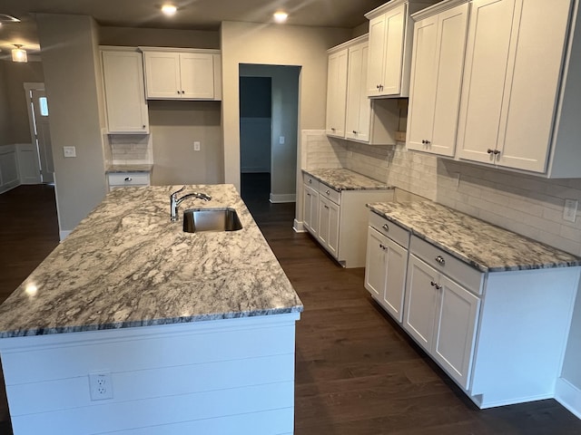 kitchen with stone countertops, dark wood-type flooring, white cabinets, a kitchen island with sink, and a sink