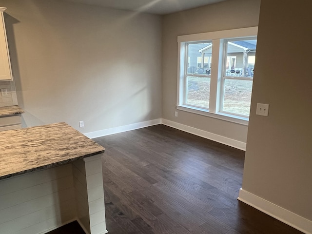 unfurnished dining area featuring baseboards and dark wood-type flooring