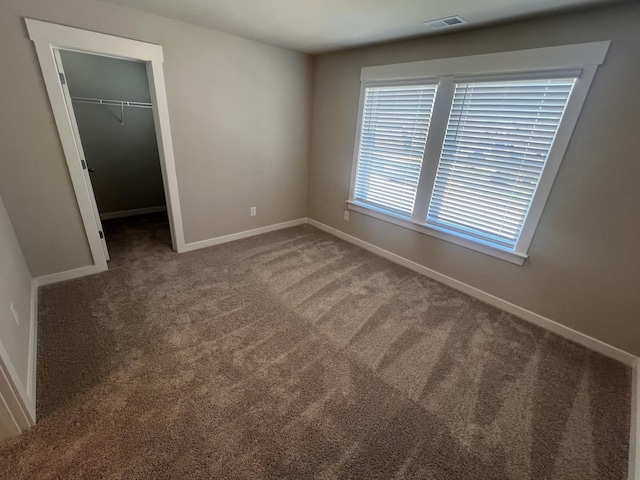 unfurnished bedroom featuring carpet floors, a walk in closet, a closet, visible vents, and baseboards