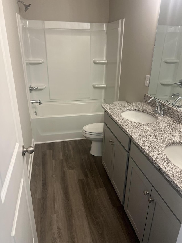 full bathroom with double vanity, shower / bathtub combination, toilet, a sink, and wood finished floors