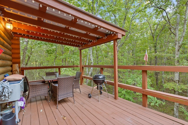 wooden deck featuring outdoor dining space, a grill, and a view of trees