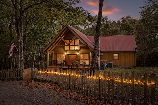 rustic home featuring a fenced front yard, metal roof, covered porch, central AC, and board and batten siding