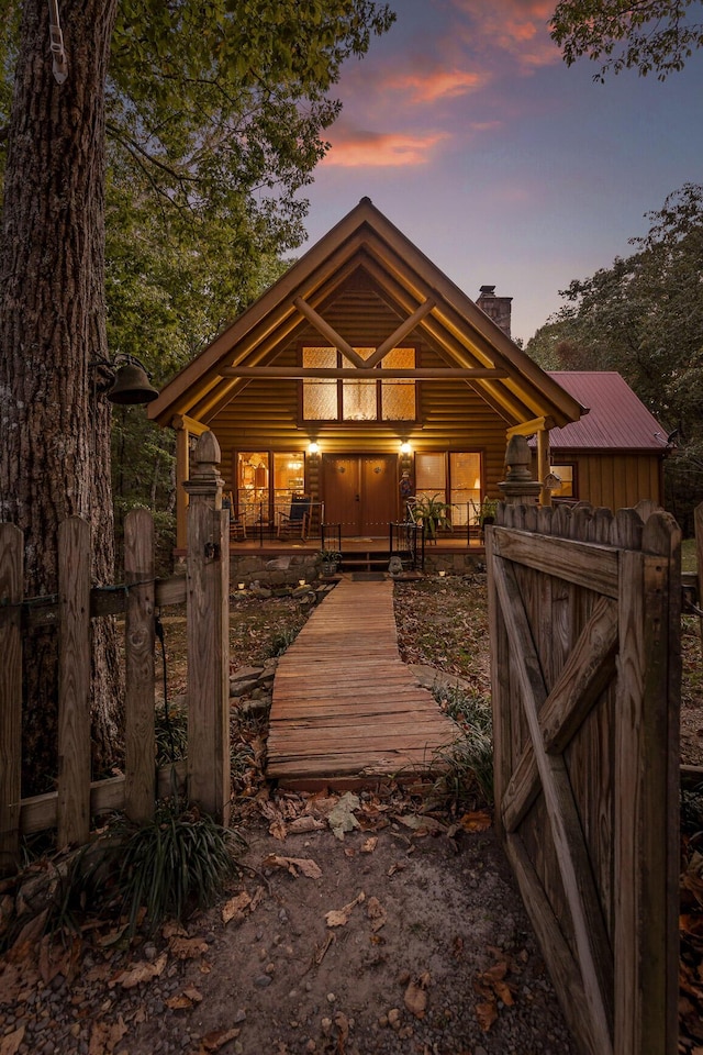 view of front of property with a chimney, metal roof, covered porch, a gate, and fence