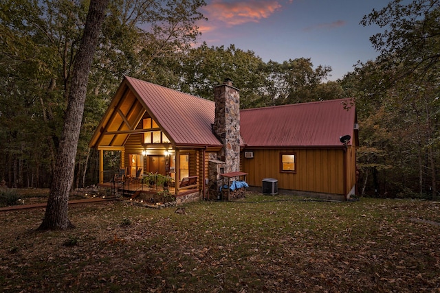 view of front of property featuring central air condition unit, metal roof, a chimney, and a front lawn