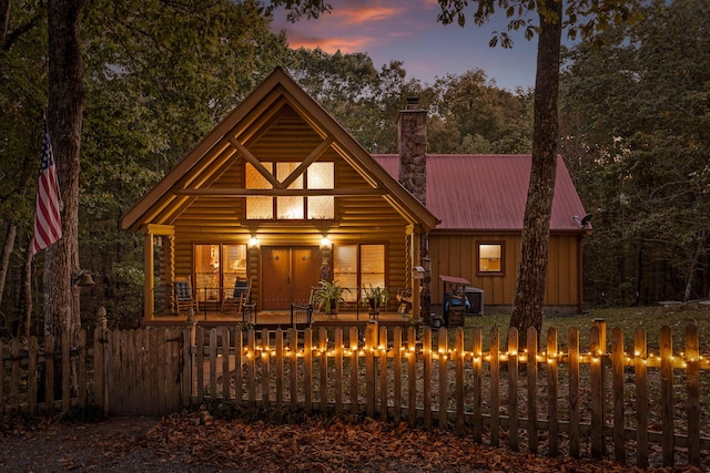 view of front facade featuring a fenced front yard, a chimney, board and batten siding, metal roof, and log siding