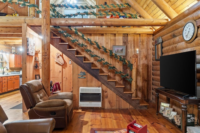 living area featuring rustic walls, stairway, heating unit, light wood-style floors, and beam ceiling