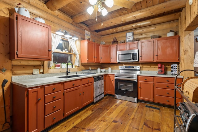 kitchen featuring stainless steel appliances, a sink, light countertops, beam ceiling, and rustic walls