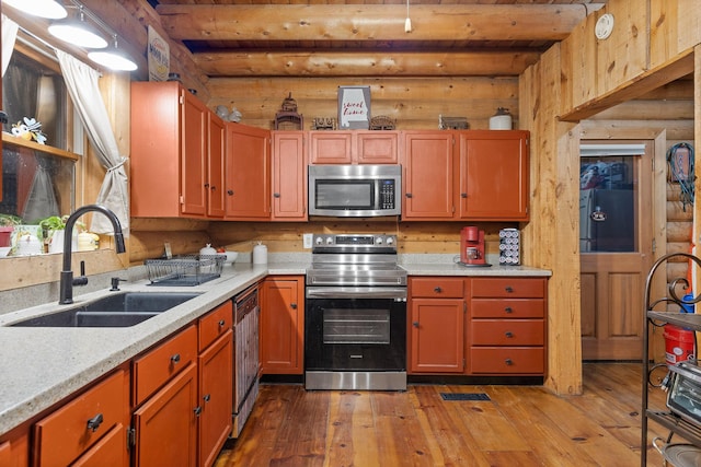 kitchen with light wood finished floors, stainless steel appliances, rustic walls, a sink, and beamed ceiling