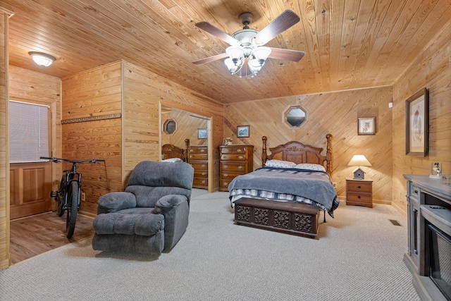 carpeted bedroom featuring a ceiling fan, wooden ceiling, and wood walls